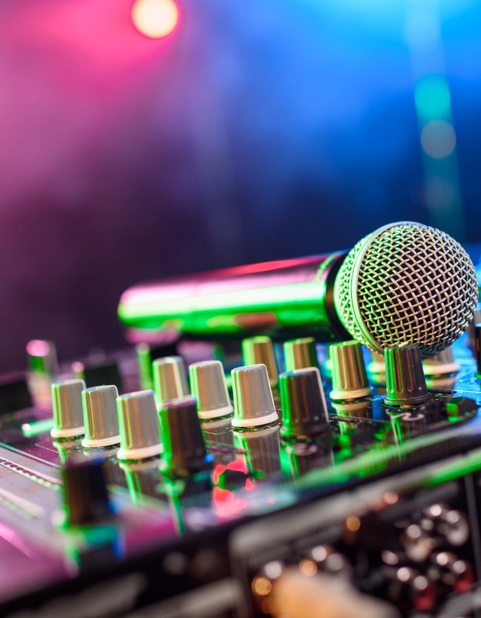 Dynamic microphone resting on an audio mixer with knobs, lit by colorful pink and blue stage lighting.