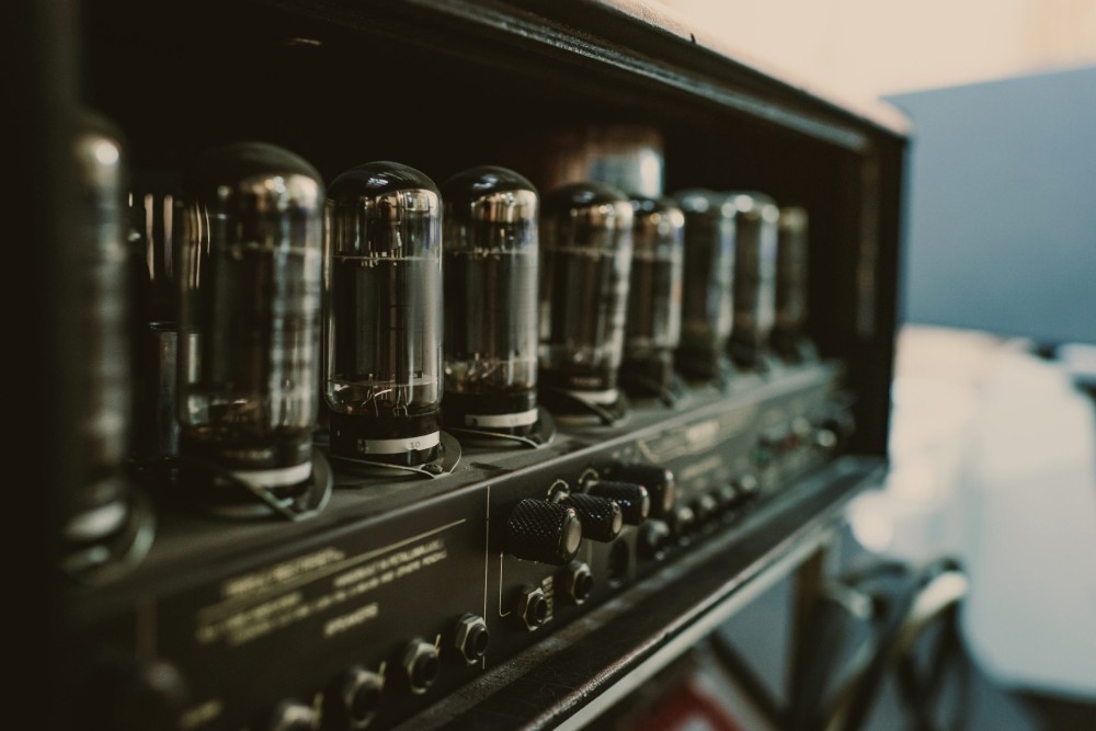 Close-up of vacuum tubes on a vintage guitar amplifier head, with control knobs and input jacks visible along the panel.