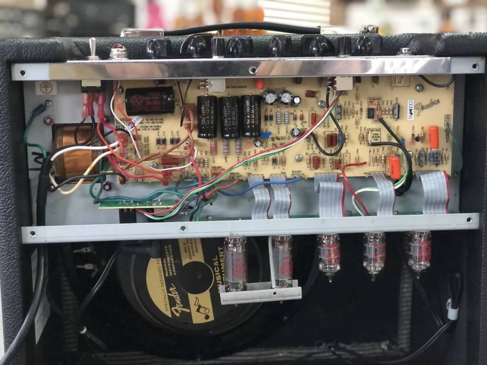 Interior of a Fender guitar amplifier showing circuit board, capacitors, vacuum tubes, wiring, and a Fender speaker.