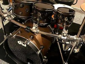 DW Drums drum kit with dark brown finish, multiple toms, kick drum with Kickport, and chrome hardware in a studio.