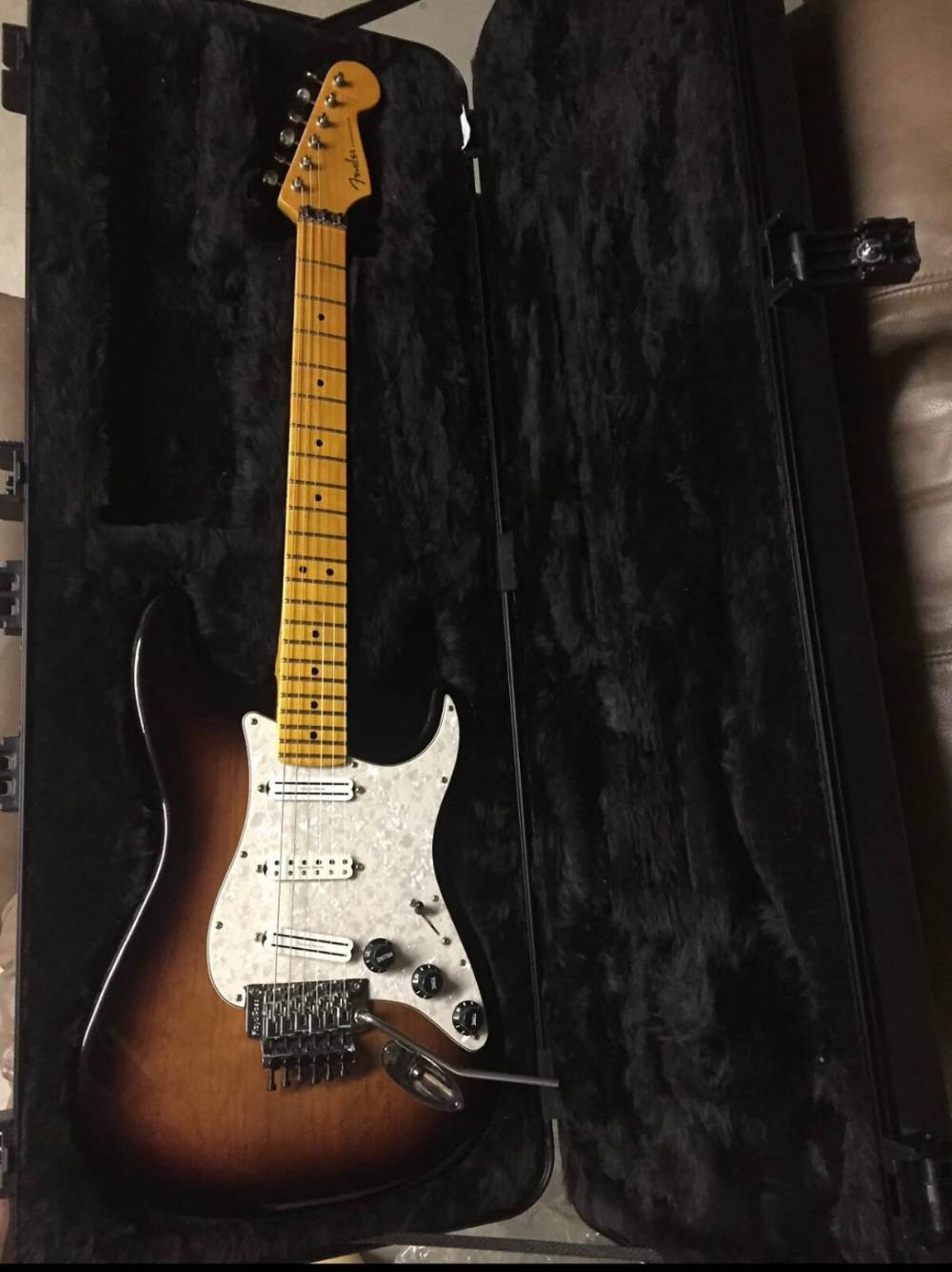 Fender Stratocaster electric guitar in sunburst finish with maple neck and pearl pickguard, stored in a black hard case.